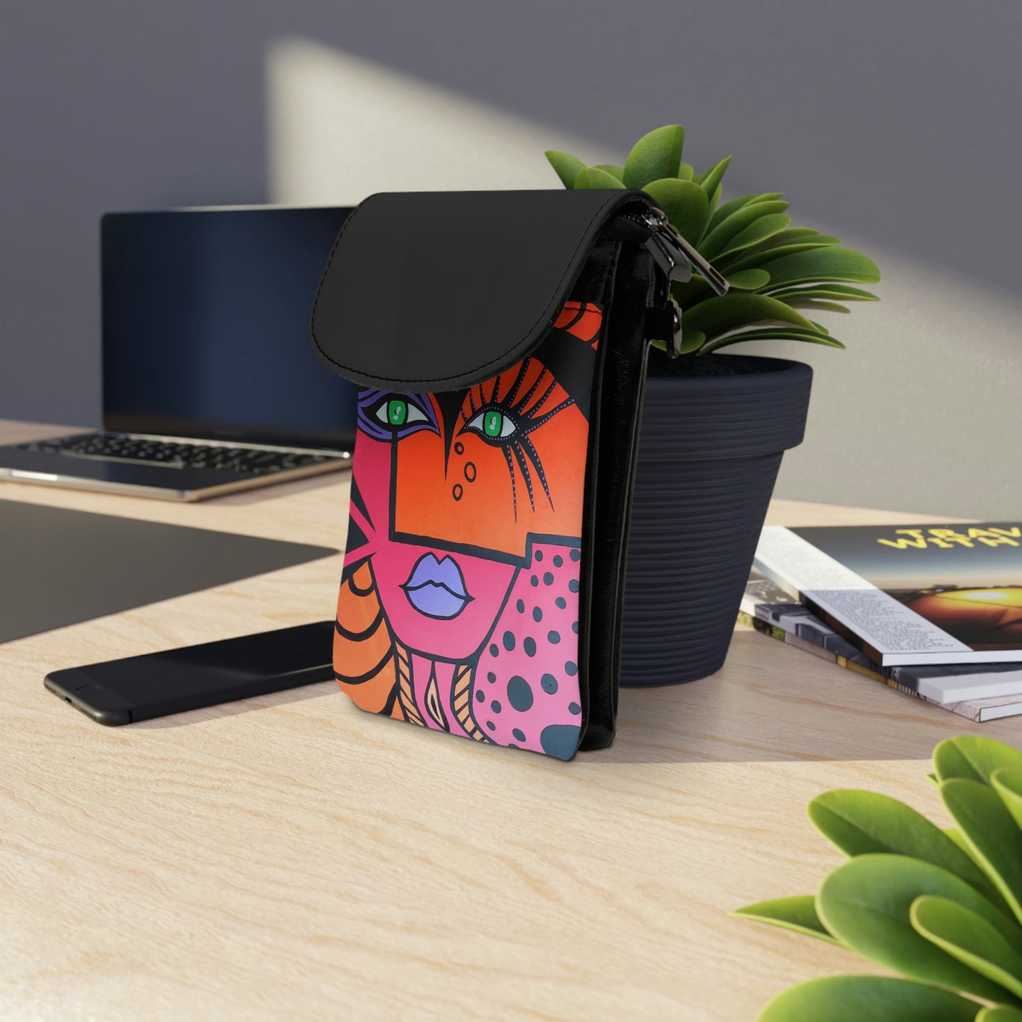 Handy Portemonnaie Woman Of Lust lehnt mit der schwarzen Kunstlederrückseite an einem Blumentopf